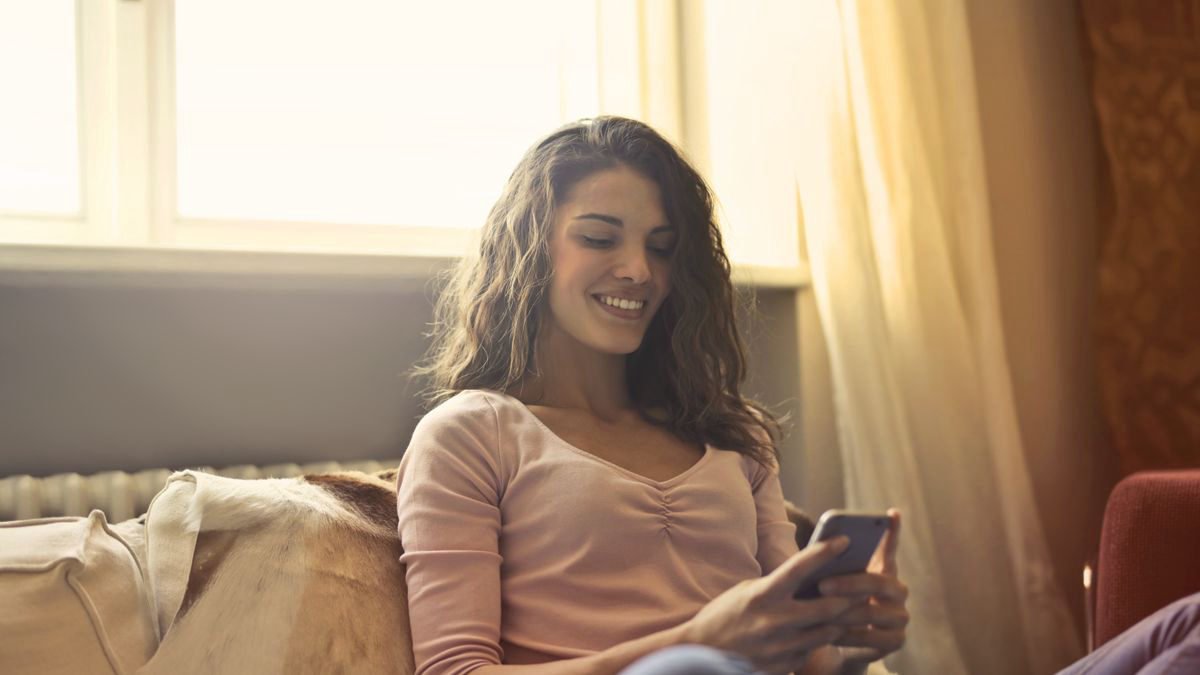 A smiling woman sitting comfortably indoors with her phone