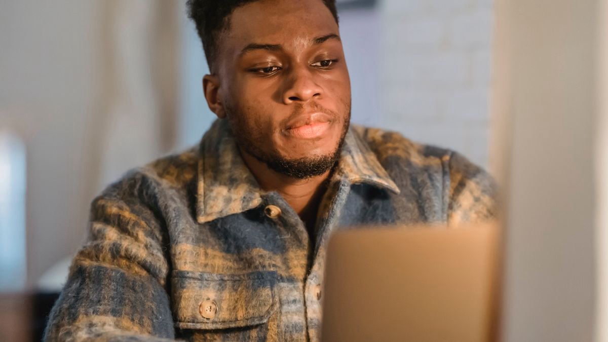 A young man working on a laptop at a desk at home