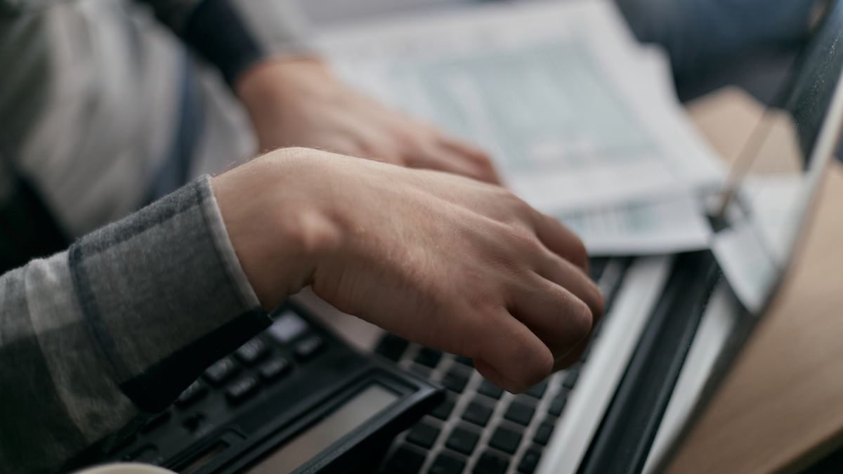 Hands working out a budget on paper next to a laptop