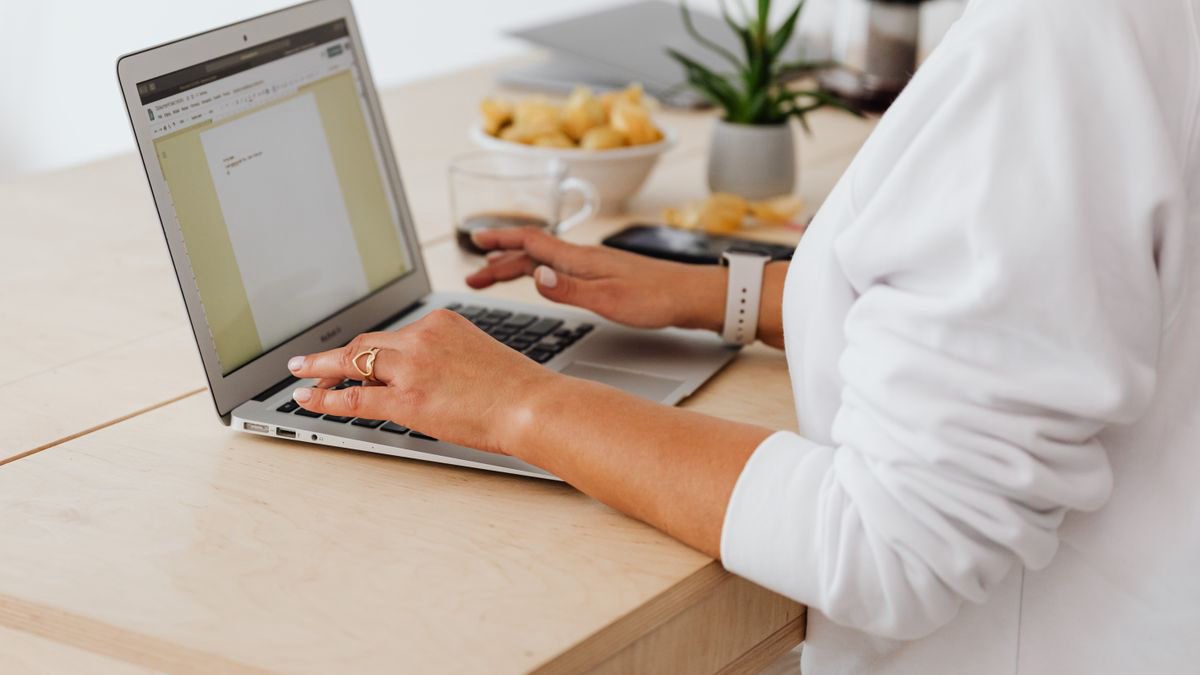 A woman typing on a laptop at a home desk with a coffee mug beside her