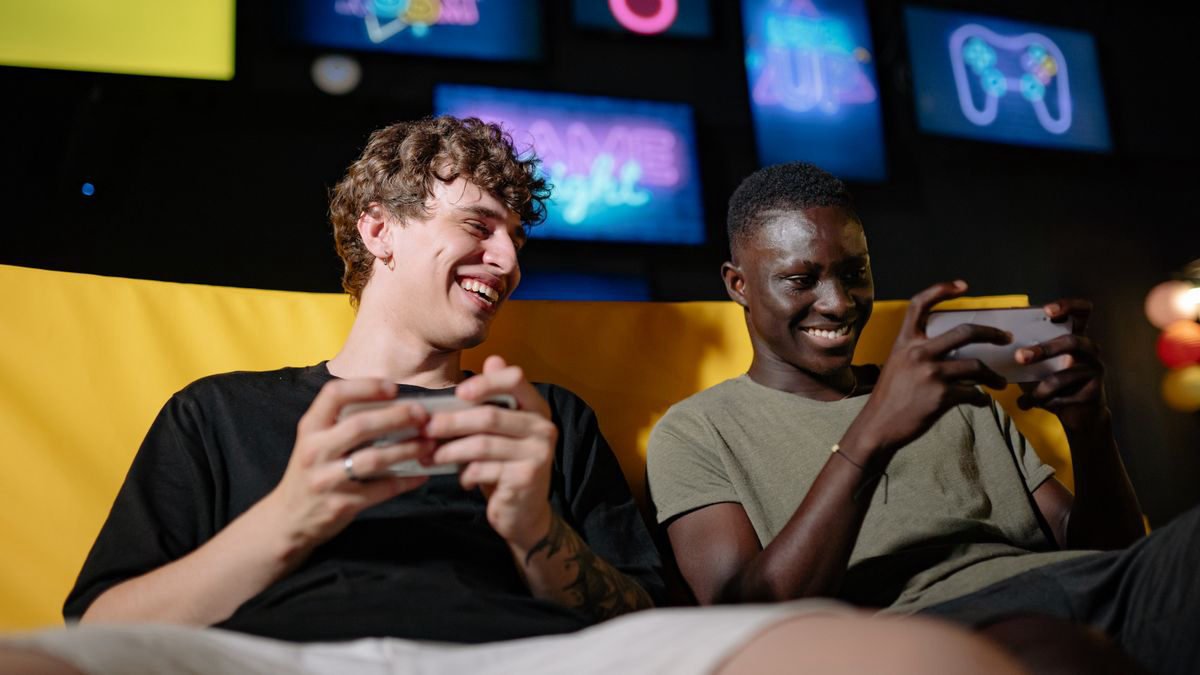 Two young men sitting together and playing games on their phones indoors