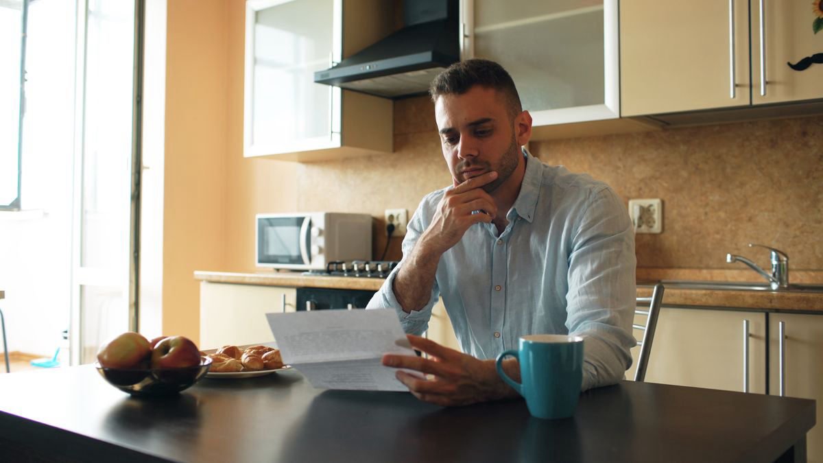 A man reading a letter at a kitchen table in morning light