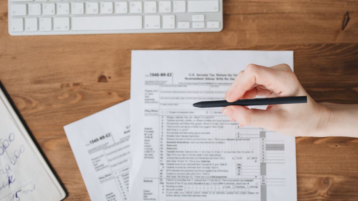 A hand holding a pen over US tax forms on a wooden table