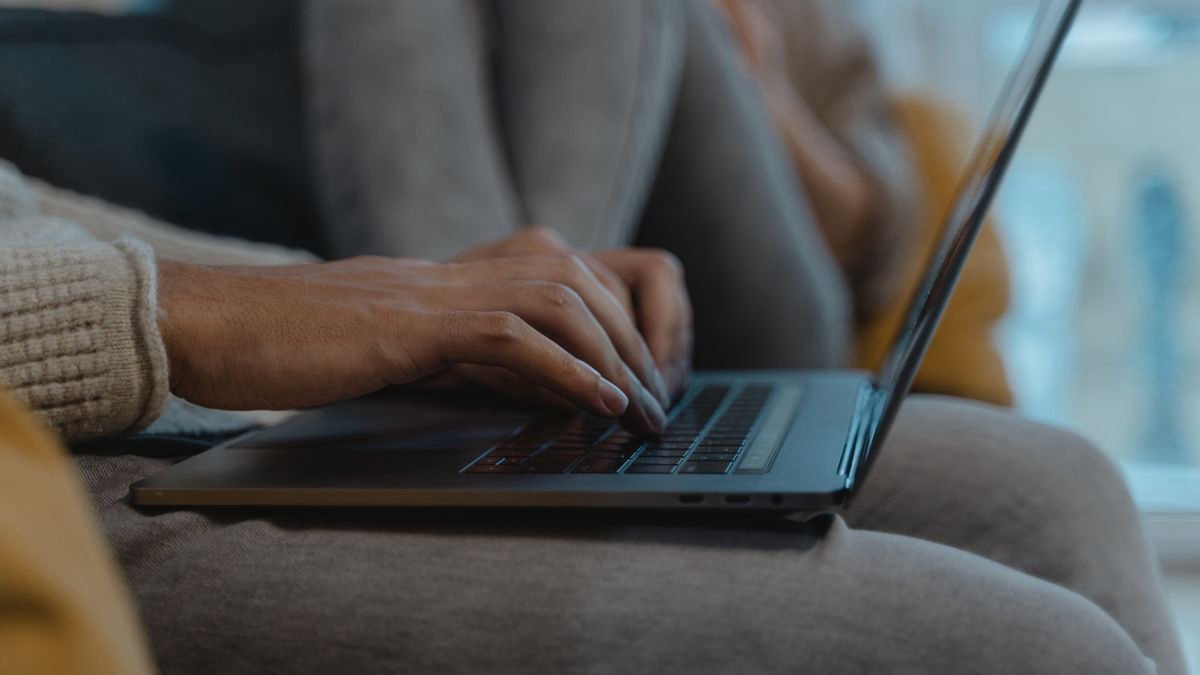 Close-up of a person's hands typing on a laptop in a cosy room