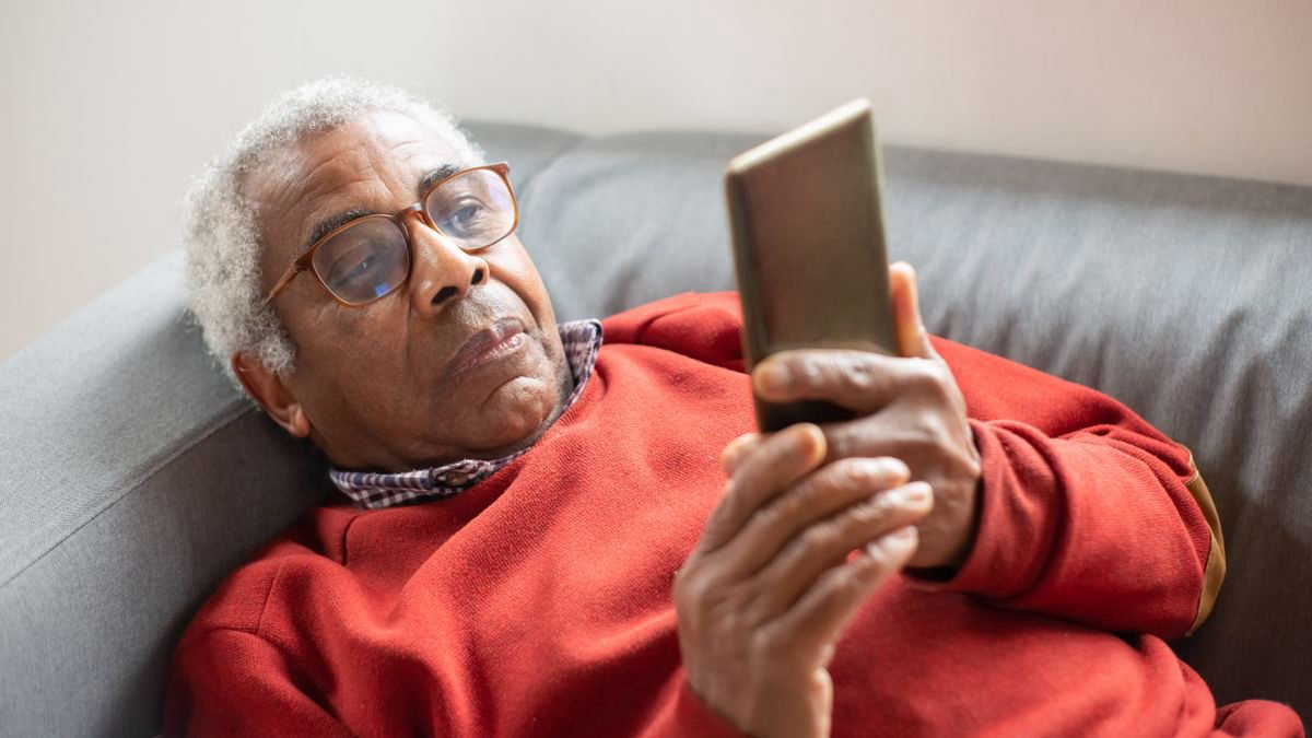Older man in glasses relaxing at home while using a smartphone